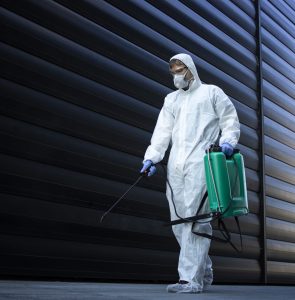 Person in white chemical protection suit doing disinfection of public areas to stop spreading highly contagious corona virus.